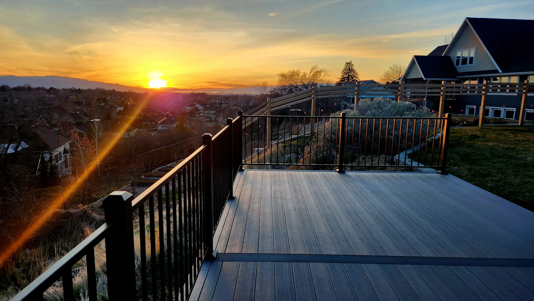 Composite backyard deck with black metal railing overlooking sunset and mountain views in Utah