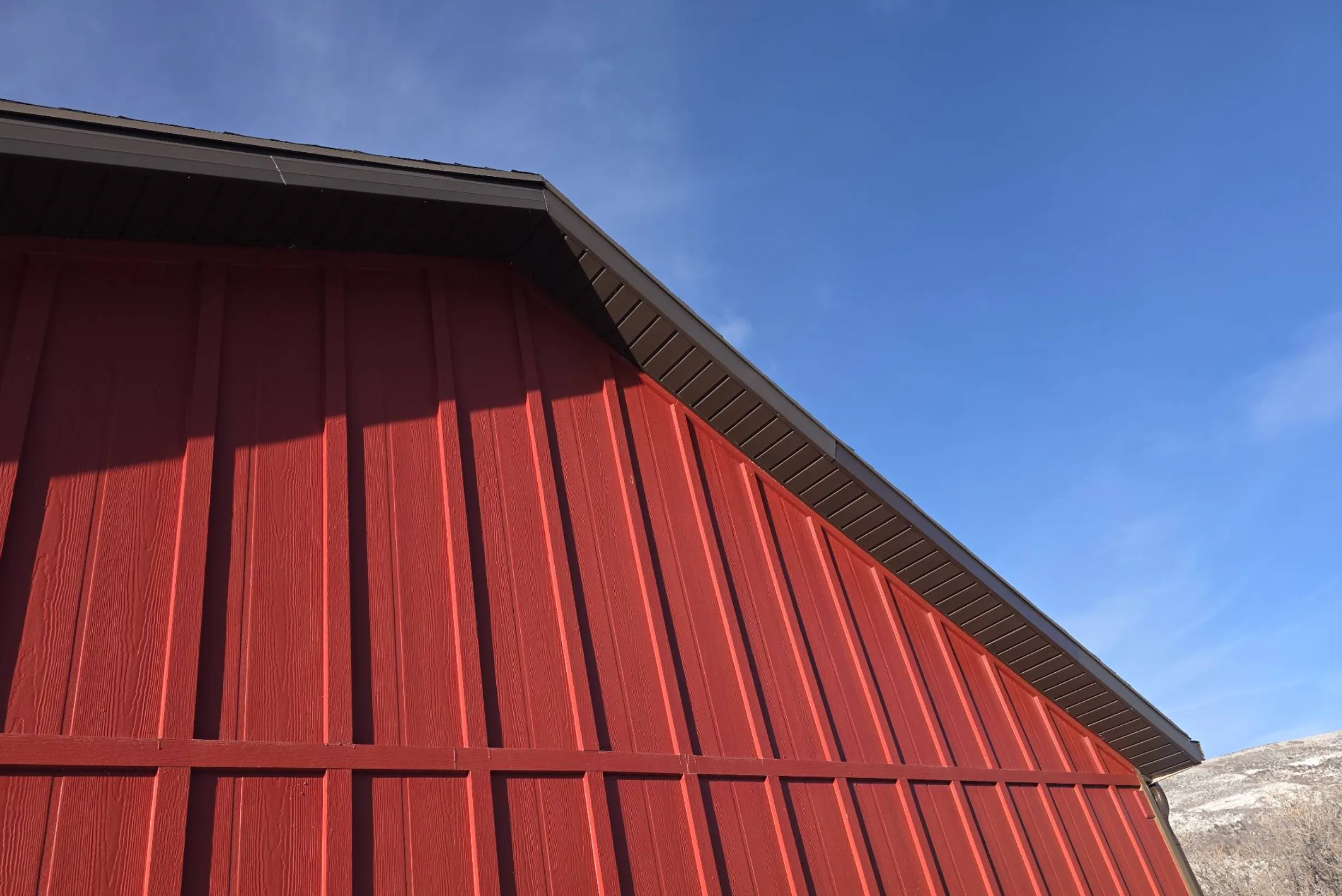 Red board and batten exterior siding with dark soffit and trim under a clear blue sky